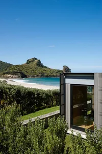 Modern, minimalist holiday home featuring a large window overlooking a serene beach and lush greenery.