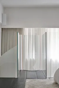 極簡室內空間，展示玻璃牆與玻璃地板，搭配淺色窗簾及木地板上的地毯