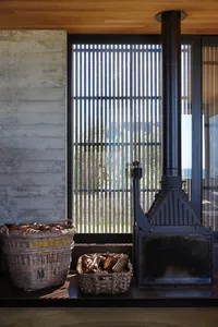 A modern industrial fireplace made of metal with a metal chimney and wood storage baskets.