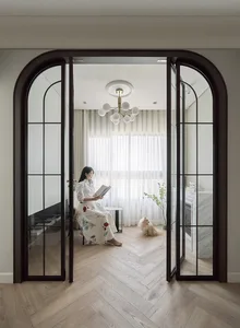 A modern living room with glass doors and a woman sitting on a sofa reading a book.