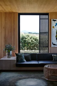 A modern living room featuring a wood paneled wall with a built-in couch, large windows providing natural light, and comforta