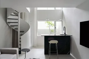 A modern minimalist living space featuring a spiral staircase, a bar with a black marble countertop, and a TV.