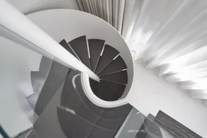 A modern wooden staircase in a white interior space with white curtains.