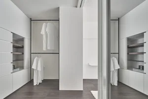 A minimalist closet with white surfaces and hanging clothes.