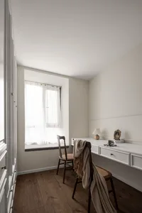 A minimalist home office with a wooden desk, white walls, and sheer curtains by the window.
