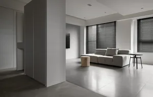 Modern minimalist living room with concrete flooring, a gray sofa, and black window blinds.
