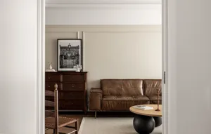 A minimalist living room with a brown leather couch, wooden coffee table, and wooden dresser.