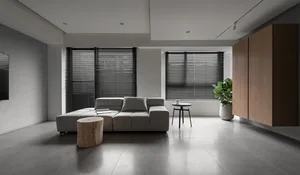 An elegant modern living room with gray minimalist furniture and concrete flooring, featuring large windows with dark blinds.