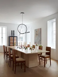 A modern dining room featuring a marble table surrounded by wooden chairs, with a minimalist pendant light fixture hanging ab