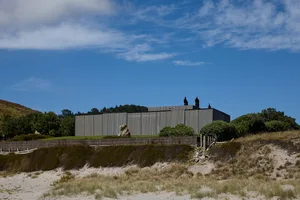 A modern metal-clad building exterior with a rectangular shape, standing on a grassy hillside with a blue sky in the backgrou