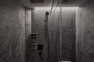 A modern minimalist bathroom with marble tiles, a glass shower enclosure, and sleek black fixtures.