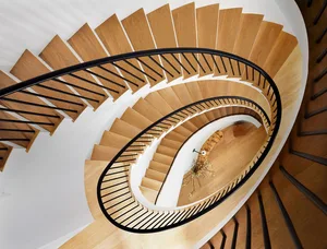 A modern, wooden spiral staircase with black railings and white walls.