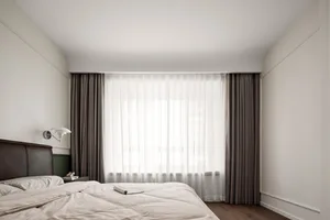 A minimalist bedroom featuring fabric curtains and wooden floors.