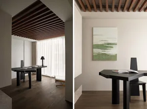 A minimalist home office space featuring black furniture, wooden ceiling beams, and a window with white curtains.