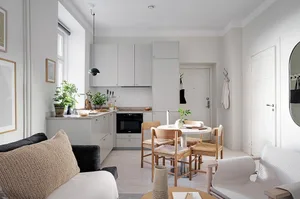 Modern, minimalist kitchen with neutral-colored cabinets, black appliances, and light wooden furniture.
