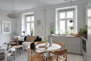 A minimalist residential space featuring a white dining table surrounded by wooden chairs, a grey sofa with white cushions, a