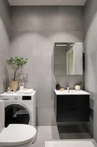 A modern bathroom with concrete tile walls, white appliances, and black cabinetry