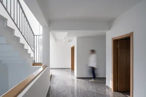 A modern corridor with concrete flooring and white walls, showing a blurred figure walking.