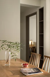 Modern dining room with wooden table, chairs, and a vase of greenery.