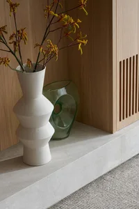 Modern empty space featuring a wooden cabinet and ceramic vase with flowers.