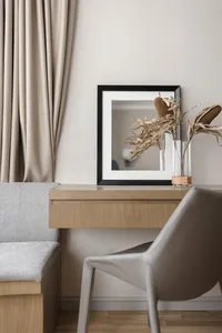 A modern interior workstation featuring a minimalist wooden desk with a black-framed mirror and dried plant decoration.