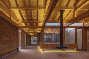 Modern living room with wooden ceiling beams, large windows, and a central fireplace.