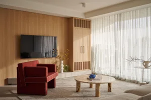 A modern living room featuring wooden walls, red armchairs, a marble coffee table, and white sheer curtains.