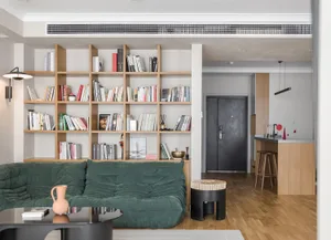 A modern minimalist living room featuring wooden shelves filled with books and decorative items, with a green sofa and a wood