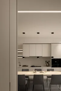A modern minimalist kitchen with white cabinets, pendant lights, and a dining table.