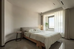 Modern minimalist bedroom with light neutral tones, featuring a comfortable bed with a simple wooden frame and upholstered he