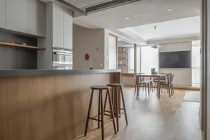 A modern kitchen featuring wooden cabinets and stools, metal accents, and a minimalist design.