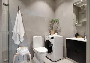 Modern minimalist bathroom with concrete walls, white toilet, white washing machine, black sink cabinet, and white towels.