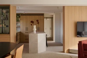 A modern residential interior featuring wooden cabinets and a marble column with a vase of flowers.