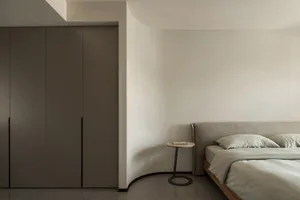 A minimalist bedroom with neutral-colored furniture and walls, featuring a bed with a low-profile headboard and a simple side
