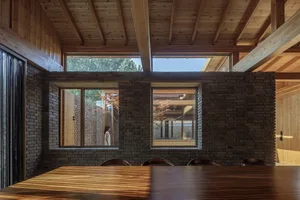 A minimalist interior space featuring brick and concrete materials with a wooden table and large windows.