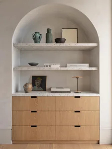 A modern wooden cabinet with marble shelves containing decorative items and books.