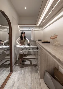 A woman using an ironing board in a modern closet with wooden cabinetry and a decorative cat statue.