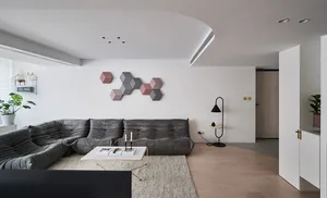 A modern living room featuring a gray sofa, minimalist decor, and a hexagonal art piece on the wall.