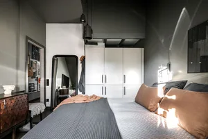 A minimalist bedroom with mixed materials, featuring a bed with grey and brown bedding, and a white wardrobe.