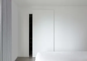 A minimalist bedroom with a white wall, bed, and sliding door.