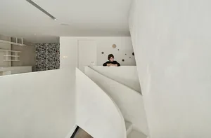 A minimalist interior featuring a concrete staircase with a white wall and a person leaning against the wall in the backgroun
