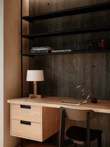 A minimalist home office featuring wooden furniture and a bookshelf with books and decorative items.