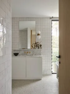 Modern bathroom with marble tiles, white cabinetry, and a sink with brass fixtures.