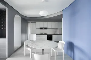 A modern kitchen and dining room with white marble table and chairs, white walls, and white cabinets.