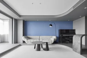 Modern living room with white furniture, blue accent wall, and black and white coffee tables.