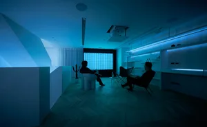 Two individuals sitting in a modern living room with metallic elements and a blue light setting.