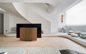 A modern living room with minimalist design, featuring hardwood flooring, a wooden cabinet, and a comfortable seating area.