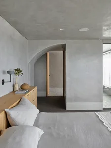 A minimalist bedroom with concrete walls and a light-colored bedspread.