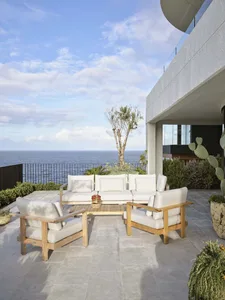 A modern minimalist outdoor patio featuring a comfortable seating area with white cushions and wooden furniture, set against 