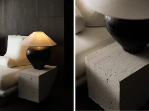 A lamp with a textured ceramic base and a white conical shade, placed on a rough-cast cement block, beside a plush white sofa